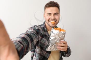 Handsome young man taking selfie with tasty potato chips on light background�