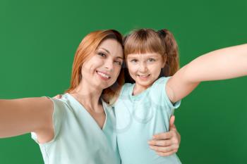 Woman and her little daughter taking selfie on color background�