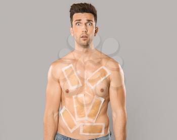 Shocked young man with wax strips on his body against grey background�