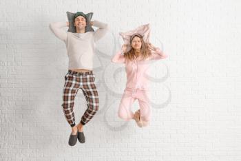 Jumping young couple in pajamas and with pillows on white brick background�