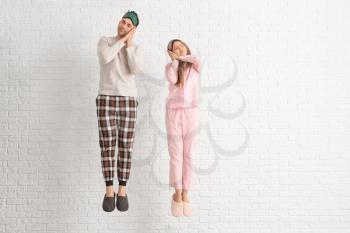 Jumping young couple in pajamas on white brick background�