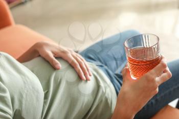 Young pregnant woman drinking alcohol at home�