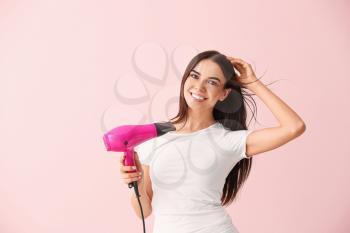 Beautiful young woman with hair dryer on color background�