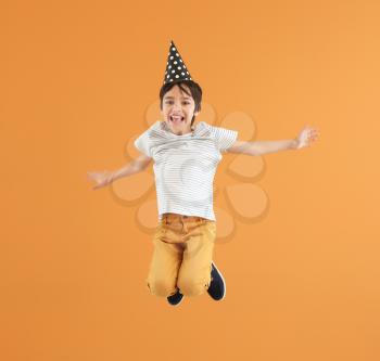 Jumping little boy with party hat on color background�
