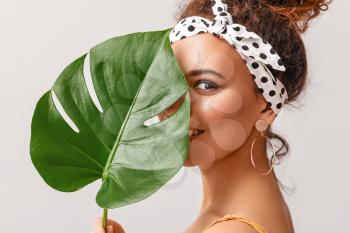 Beautiful African-American woman with tropical leaf on light background�
