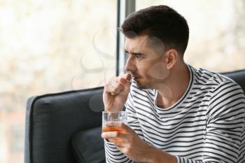 Depressed young man drinking alcohol at home 