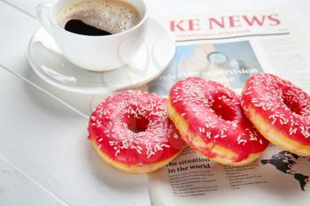 Sweet tasty donuts, cup of coffee and newspaper on white wooden background�