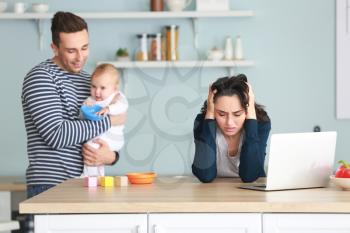 Happy father with his baby and wife suffering from postnatal depression in kitchen�