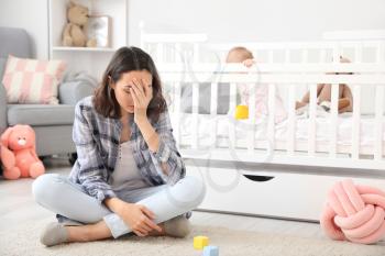 Young woman suffering from postnatal depression near bed with baby at home�