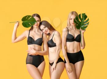 Beautiful young women in underwear and with tropical leaves on color background�