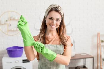 Young housewife putting on rubber gloves before cleaning flat�