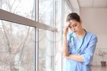 Depressed female doctor near window in clinic�