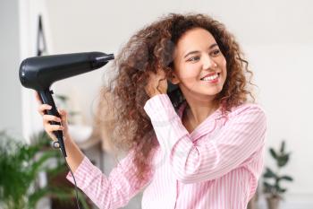 Beautiful young African-American woman with blow dryer at home�