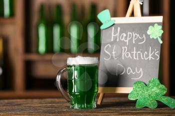 Mug of green beer and board with text HAPPY ST. PATRICK'S DAY on wooden table�