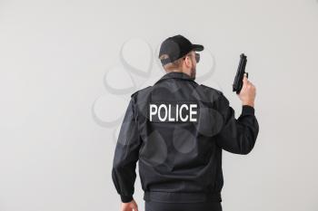 Male police officer with gun on light background�