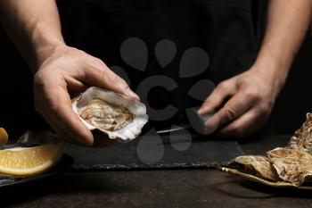 Man opening shell of fresh oyster on dark background�