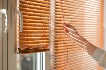 Woman opening blinds on window�