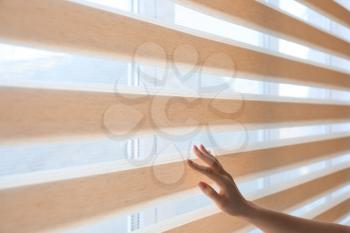 Woman opening blinds on window�