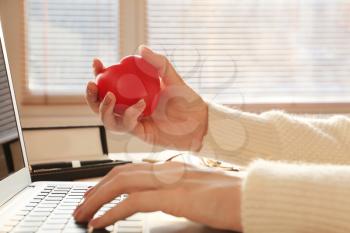 Woman squeezing stress ball while working with laptop in office�