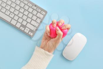 Female hand with stress ball, computer keyboard and mouse on color background�
