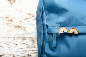 Backpack with pinned rainbow badges as a symbol of LGBT on white wooden background�