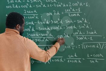 African-American math teacher writing on blackboard in classroom�