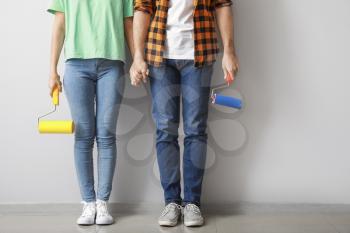 Young couple with paint rollers near light wall in new apartment�