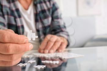 Senior man with Parkinson syndrome doing puzzle at home, closeup�