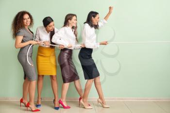 Young women pulling rope against color wall. Concept of feminism�