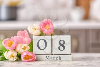 Calendar with date of International Women's Day and flowers on table in kitchen�