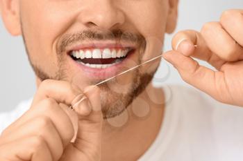 Handsome man flossing teeth on grey background, closeup�