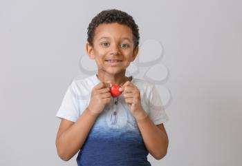 Little African-American boy with red heart on grey background. Concept of donations�