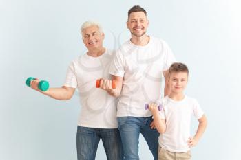Man with his father and son holding dumbbells on color background�