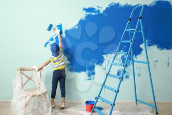 Little African-American boy painting wall in room�