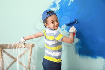 Little African-American boy painting wall in room�