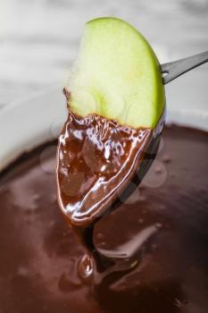 Dipping of tasty apple into bowl with chocolate fondue, closeup�