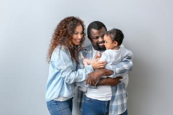 Happy African-American parents with cute baby on white background�