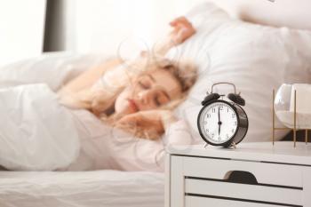 Alarm clock on table of sleeping young woman in bedroom�