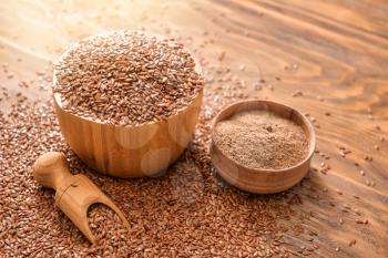 Bowls with flax seeds, powder and scoop on wooden background�