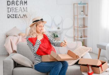 Happy young woman unpacking box with new clothes at home�