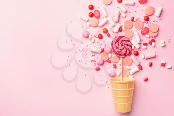 Wafer cup with tasty candies on color background�