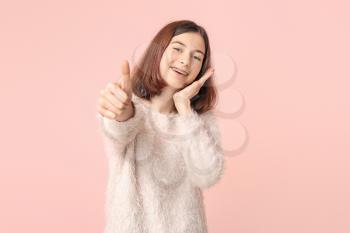 Teenage girl with dental braces showing thumb-up gesture on color background�
