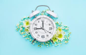 Alarm clock with flowers on color background�