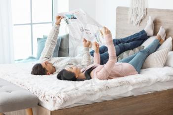 Happy young couple reading newspaper in bedroom�