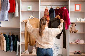 Woman choosing winter clothes near wardrobe�