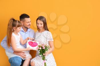 Husband and little daughter greeting woman to Mother's Day on color background�