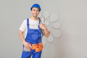 Handsome male worker with cables on grey background�
