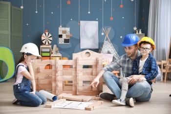 Father and little children dressed as builders playing with take-apart house at home�