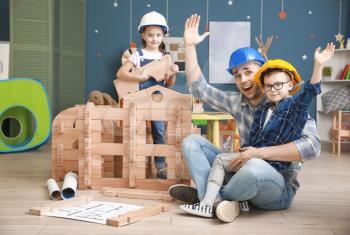 Father and little children dressed as builders playing with take-apart house at home�