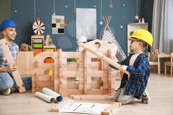 Father and little son dressed as builders playing with take-apart house at home�